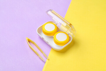Container with contact lenses and tweezers on color background