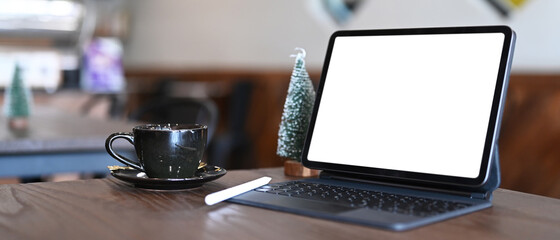 Comfortable workspace with computer tablet, coffee cup and Christmas tree on wooden table.