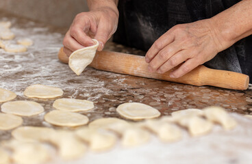 Woman rolls the dough with a rolling pin on the table.
