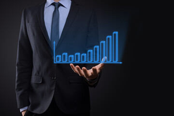 Business man holding holographic graphs and stock market statistics gain profits. Concept of growth planning and business strategy. Display of good economy form digital screen.