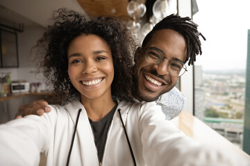 Close up portrait of smiling young African American man and woman have fun make selfie at home...