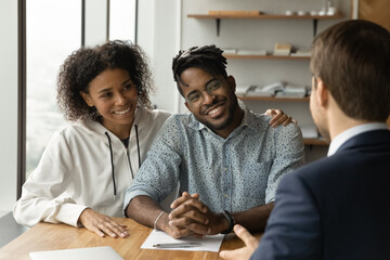 Smiling biracial man and woman talk with male real estate agent at office meeting. Happy African...