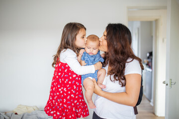 Happy woman and a little girl holding and kissing an adorable baby