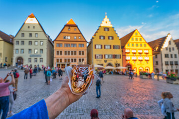 Tourist concept of hand holding waffle covered with ice cream and fruits near the town square of...