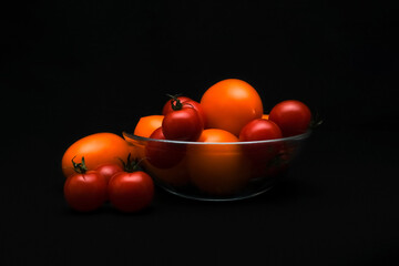 Variety of tomatoes in glass bowl on dark background