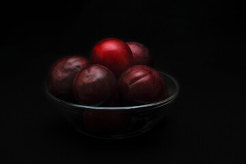 Fototapeta na wymiar Ripe purple plums in glass bowl on dark background