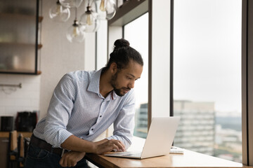 Focused millennial African American businessman look at laptop screen consult client or customer online. Serious young biracial man work on computer in office, browse wireless internet on gadget. - Powered by Adobe