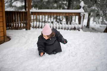 Fototapeta na wymiar Happy little girl wearing an oversized jacket and playing on the snow