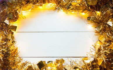 Festive frame made of gold garland with lights and tinsel on a white wooden background, copyspace....