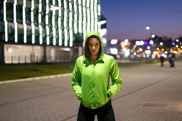 Fit woman in sport jacket on the street exercise with ciity lights on background