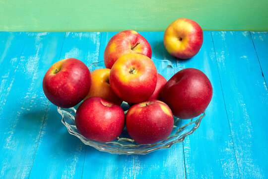 Bright red and yellow apples in a vase on a blue background.
