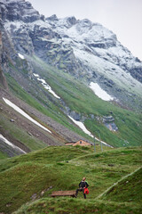 Obraz premium Man standing near wooden bench in mountain village. Beautiful view of high rocky hills with male traveler. Concept of traveling, hiking, climbing and active leisure.