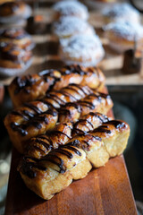 Selected Focus of Many fresh bread on a wooden table. Many diverse bread on a wooden board. Variety of breads displayed at bakery shop. Fresh from the oven pastry on wooden table.