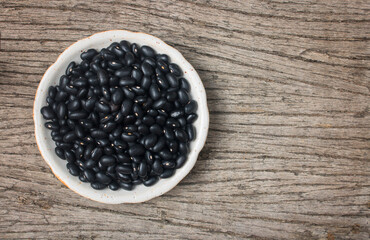 Black beans in a ceramic bowl on wooden background.