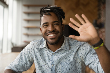 Close up headshot portrait of smiling young African American man wave greet talking on video call....