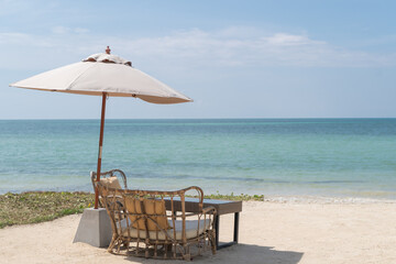 A Table with chairs and umbrella set up for a romantic meal on the beach, sky and sea in the background.