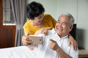 Happy old asian senior couple using smartphone for video call, selfie, taking photo