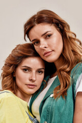 Close up portrait of two attractive young girls, twin sisters looking at camera, posing together isolated over light background