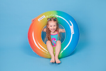 Little girl in swimsuit with inflatable ring having fun on blue background