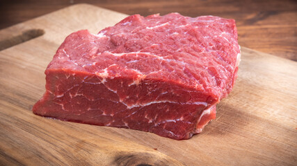 Piece of fresh raw beef on wooden kitchen cutting board