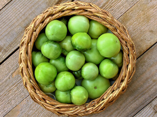 Green tomato (unripe) in wicker basket on wooden background. Unripe green tomato in bowl for fried dish or salted pickled vegetables. Raw green tomato on table for dinner