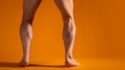 Muscular men's legs in squat, swing leg muscles, exercise. Parts of the body, yellow background