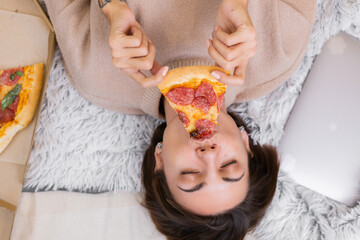 Fototapeta na wymiar Woman east fast food from delivery on bed in bedroom at home at christmas new year time. Female alone enjoying fat food, pizza. Hungry for carbs. 