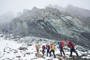 Group of male alpinists with backpacks and trekking sticks having winter hiking tour in mountains,...