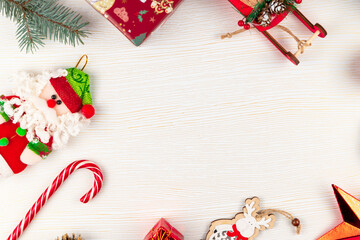 toy sleigh of santa claus, figurine of a deer, christmas tree branch, cones, bell, toy santa claus and lollipop staff on a background of white wood with gold veins