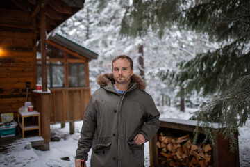 Handsome man standing with a cabin and snowy pines as background