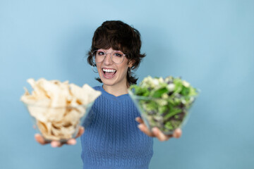 Young beautiful woman holding nachos and healthy salad over isolated blue background smiling with a happy and cool smile on face showing teeth