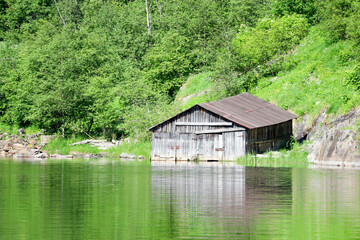 Fototapeta na wymiar picturesque old wooden boat sheds on the river with forest on the background