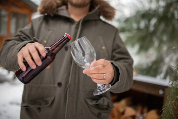 Man pouring beer into a glass goblet with snowy pines as background
