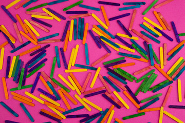 Many colorful wooden sticks on the pink background. View from above.Abstract wooden sticks background.