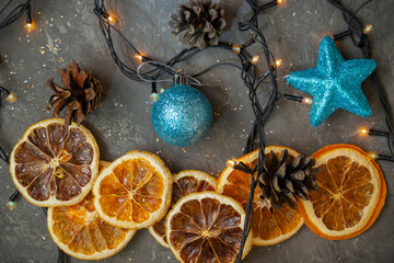 Dry circles of orange and lemon on dark concrete background in Christmas composition with garland lights. Top view, selective focus