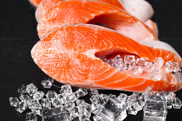 salmon sliced into pieces on a black stone board with ice cubes. red fish. fresh trout for cooking.