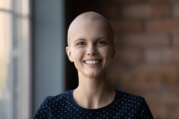 Head shot portrait smiling hairless woman looking at camera, happy young female cancer patient...