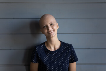 Head shot portrait smiling hairless sick woman standing on grey wooden wall studio background, optimistic cancer patient struggling with oncology disease, successful treatment and remission concept
