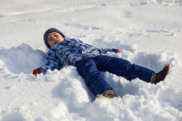 Fototapeta na wymiar happy little boy in winter clothes lies in the snow
