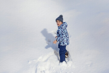Fototapeta na wymiar little boy in winter clothes standing in white snow