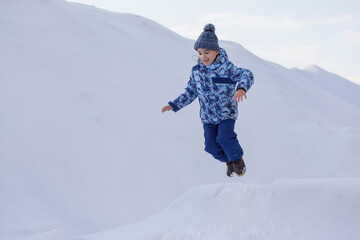 Fototapeta na wymiar little boy in winter clothes jumping in the snow
