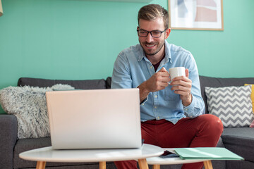 Portrait of a handsome man drinking coffee and working on a laptop remotely from home.