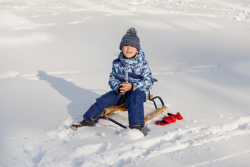 Fototapeta na wymiar little boy in winter clothes with sleigh