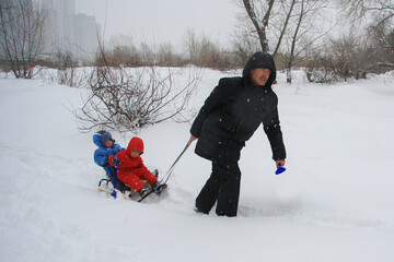 Fototapeta na wymiar Grandpa pulling his grandchildren in a sleigh in winter snowfall