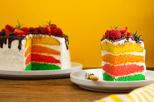 Rainbow birthday cake with fresh berries on yellow background.