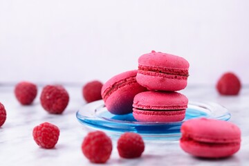 Four Raspberry macrons, two of them stacked, on blue glass plate with spilled ripe raspberries around