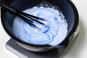 hairdresser mixes hair clarifier with a whisk in a bowl. hair dyeing process