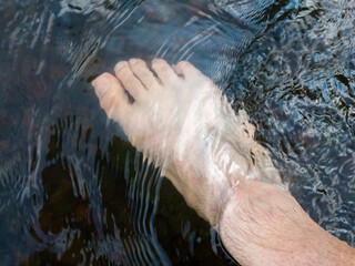 Close up human foot while stand in rapid water stream, relax in shallow creek, day off in nature,...