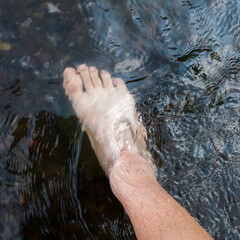 Close up human foot while stand in rapid water stream, relax in shallow creek, day off in nature,...