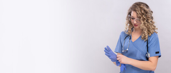 Ärztin im Kittel mit Stethoskop und Schutzbrille. 27 Jahre alt, hübsch  zieht Gummihandschuhe bei...